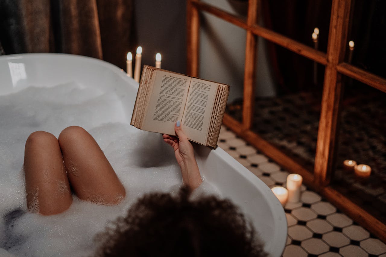 who-we-are A peaceful scene of someone enjoying a bubble bath while reading by candlelight.