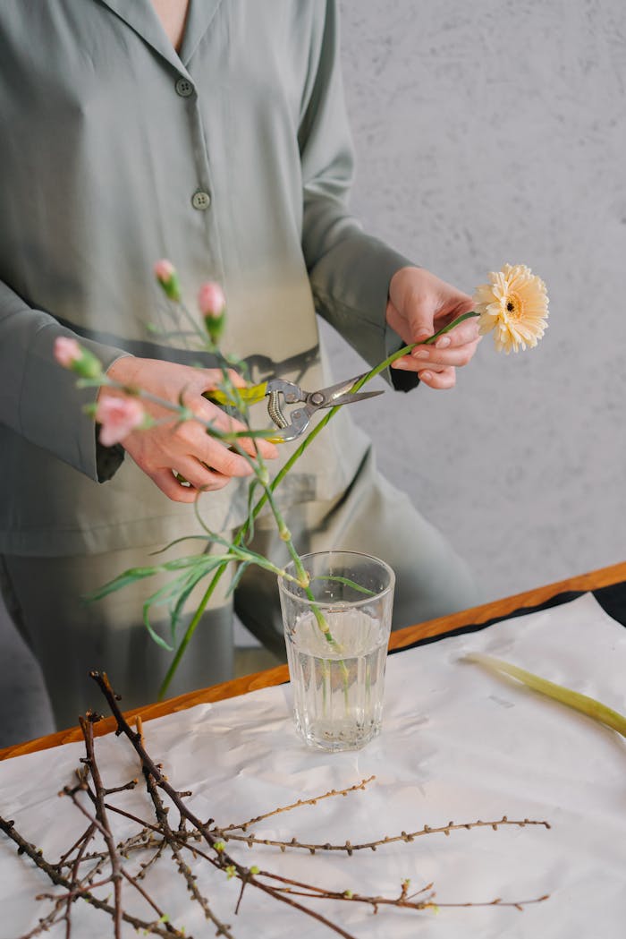 our-story A woman in green outfit trimming flowers for a floral arrangement indoors.